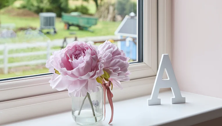 cream upvc casement window pink flower and ornimental letter A on windowcill farm machinery in the background outside - Senator Windows