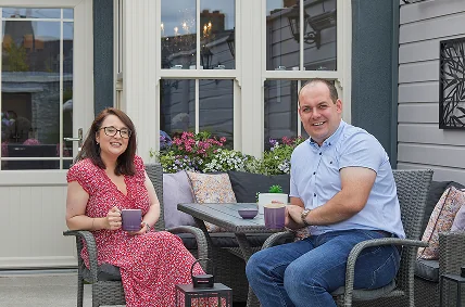 Couple relaxing with mugs beside navy sash windows on a home patio - Senator Windows