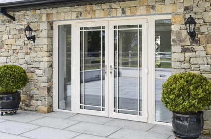 Senator French door with cream frames flanked by potted shrubs on a stone patio - Senator Windows