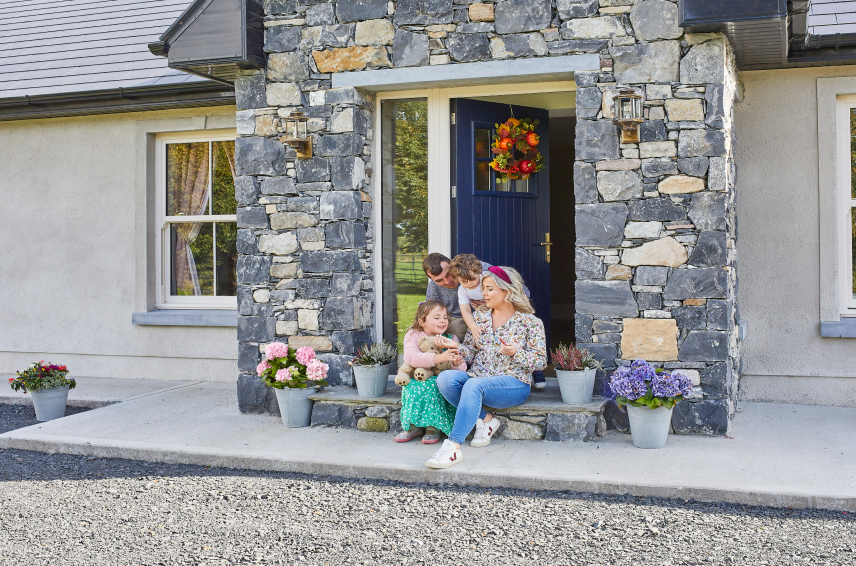 Blue composite front door with glazed sidelights at a stone-clad family home, with a family sitting outside the entrance - Senator Windows