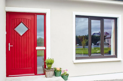Vibrant red composite door with a diamond window pane beside a dark-framed window by Senator Windows.
