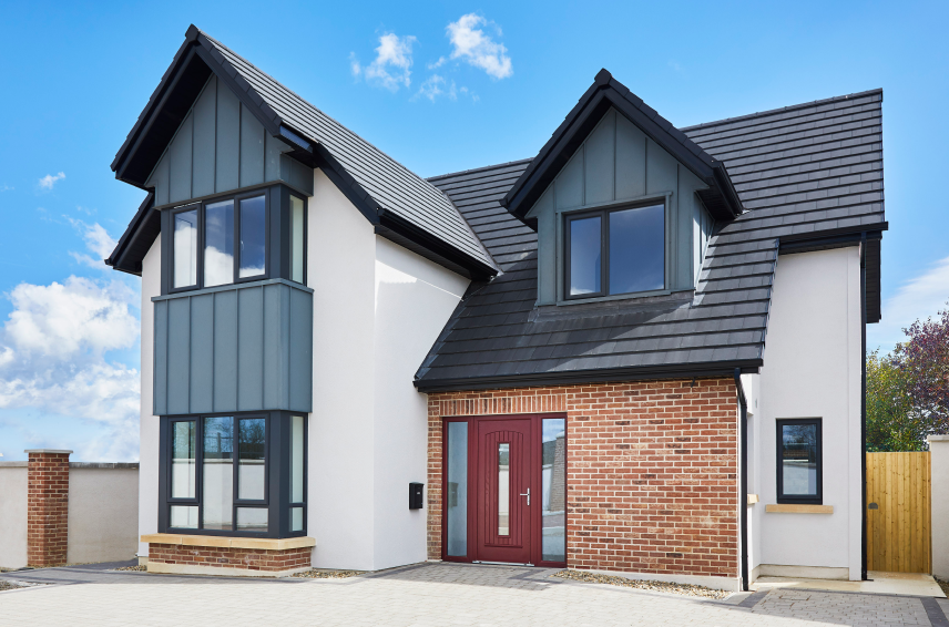 Red composite door with sidelights centered on a modern brick and white plaster home by Senator Windows.