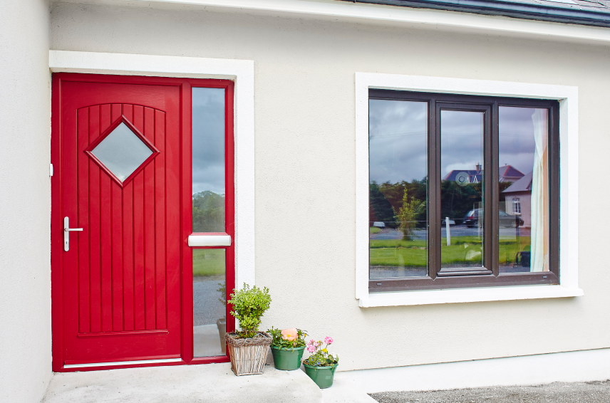 Red composite front door with diamond-shaped glazing and full-height sidelights beside a dark-framed window at a modern home - Senator Windows